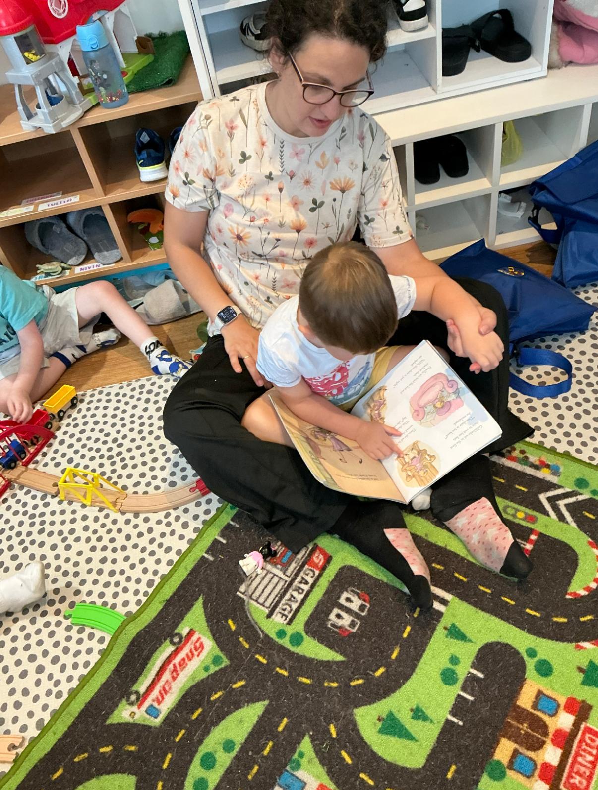 Sevjen reading a picture book with a child in the Nursery Room playroom